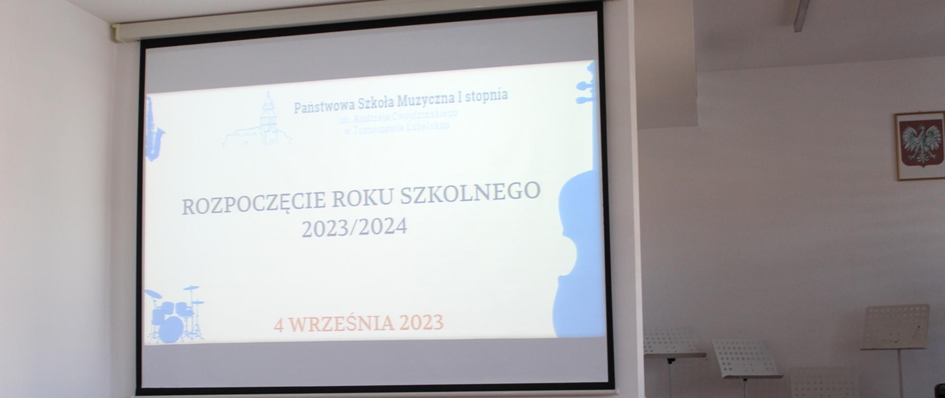 sala koncertowa szkoły, z lewej zdjęcie wyświetlane z projektora przedstawiające instrumenty muzyczne oraz informację o rozpoczęciu roku szkolnego 