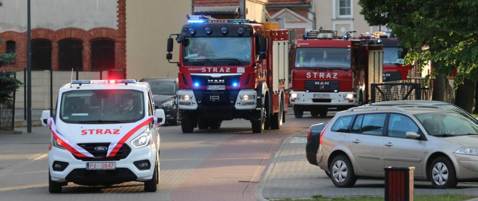 Pojazdy pożarnicze jadą w kolumnie na obchody dnia strażaka.