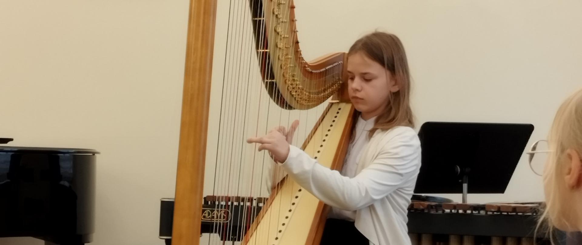 Karolina Cholewa uczennica klasy czwartej cyklu sześcioletniego wykonuje utwór na harfie.