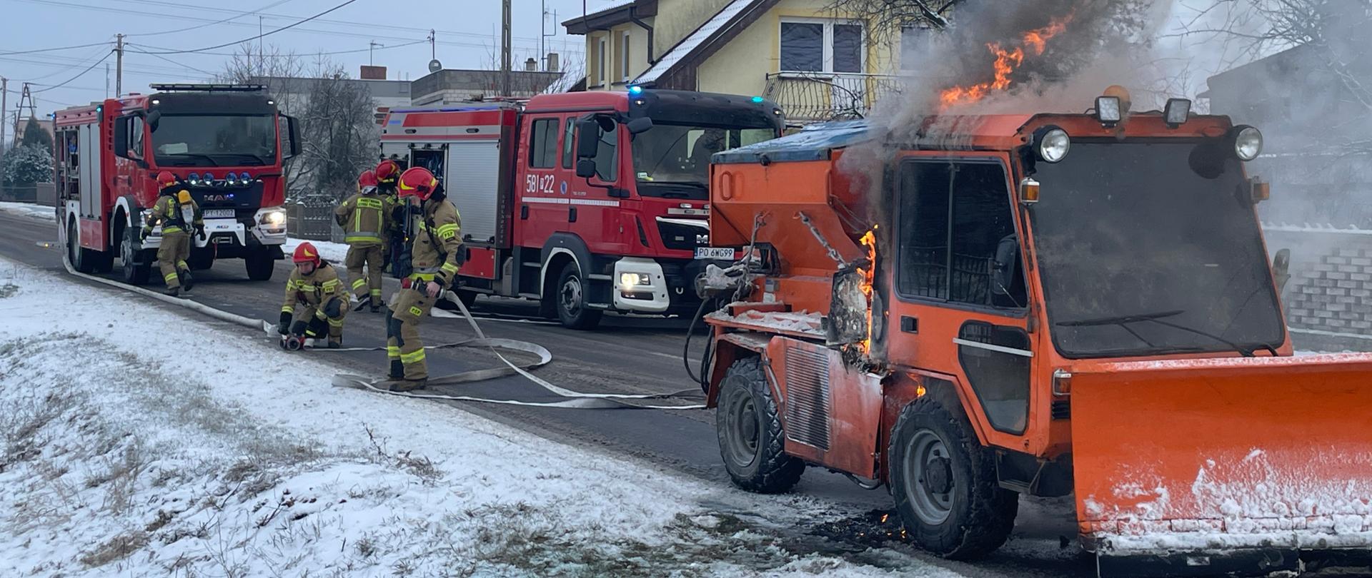 Strażacy rozwijają linię gaśniczą z przodu paląca się mała piaskarka