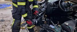 Zdjęcie przedstawia strażaka podczas rozpierania konstrukcji samochodu z użyciem narzędzi hydraulicznych.
