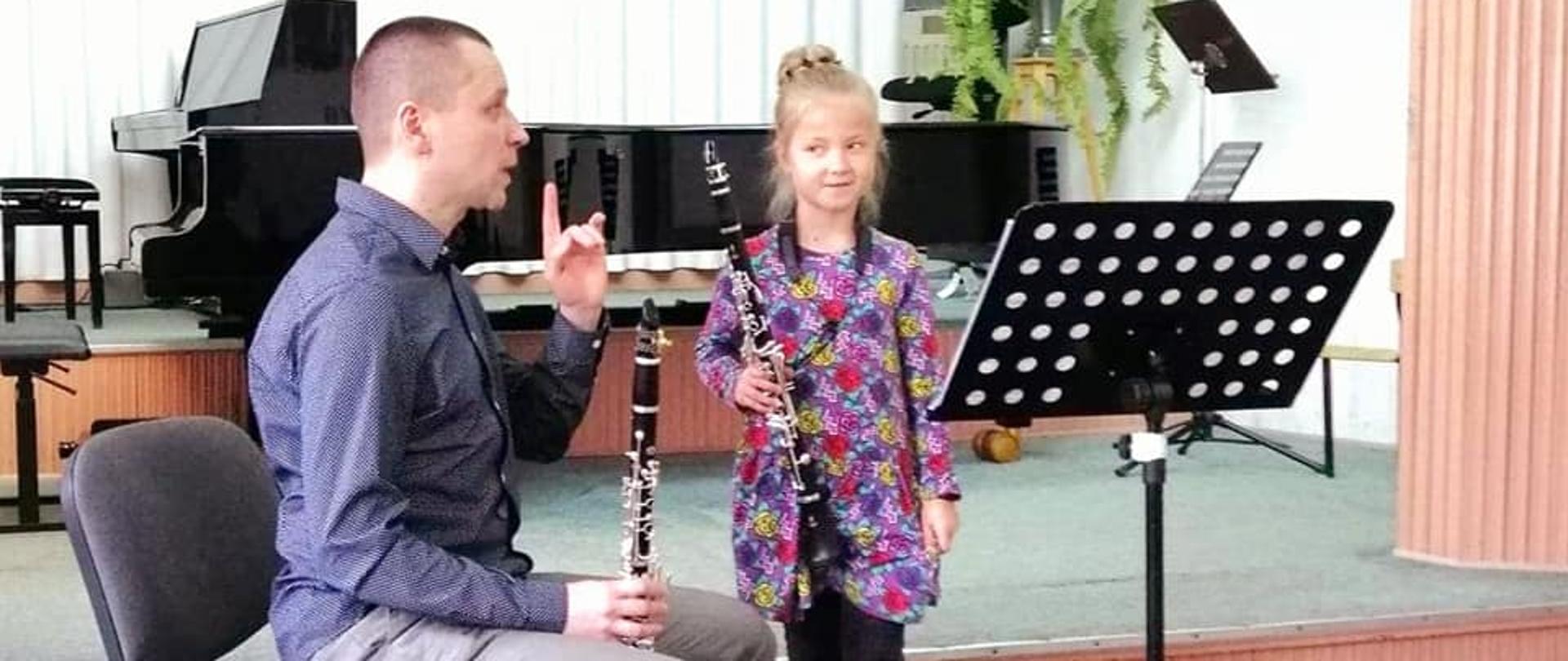 Zdjęcie - w szkolnej auli wykładowca Paweł Kroczek tłumaczy utwór dziewczynce z klarnetem