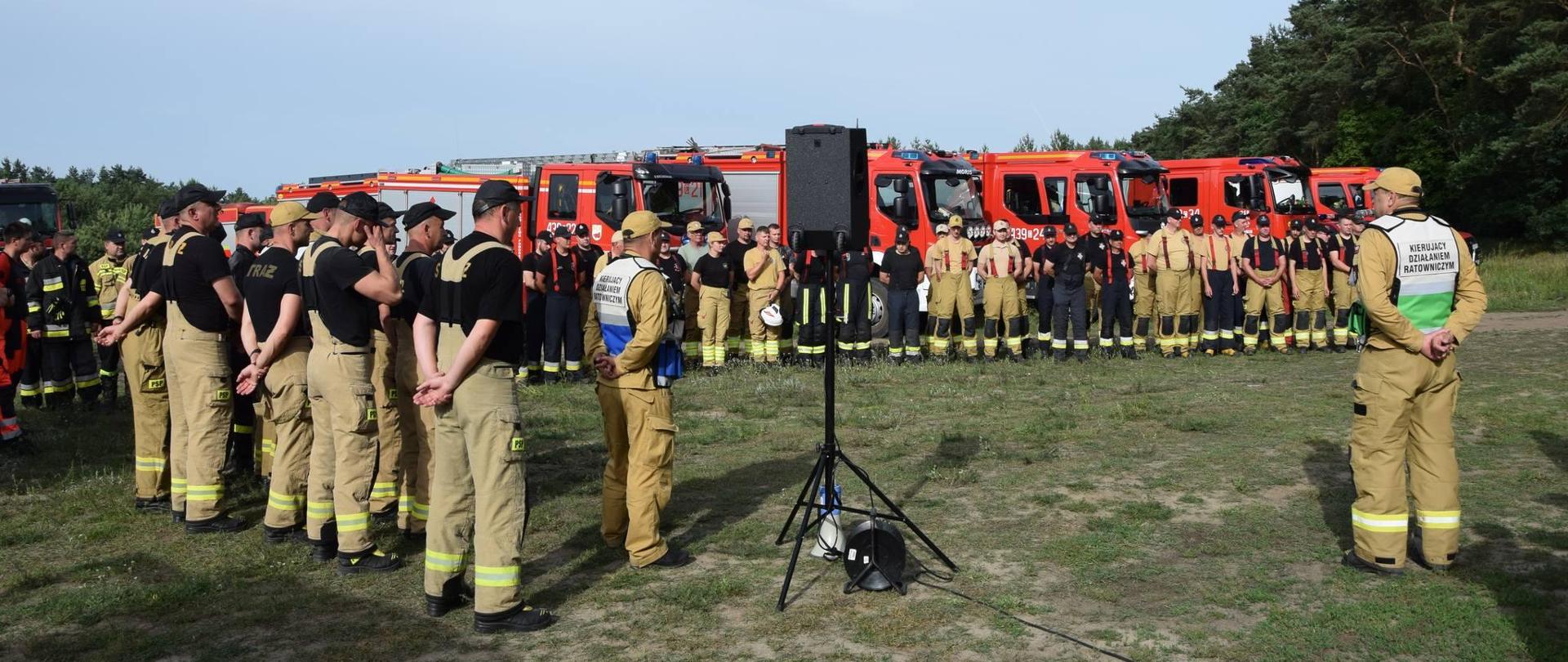 Uczestnicy ćwiczeń stoją w dwóch szeregach przed kierującym działaniami ratowniczymi.