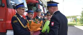 Koleżanki i koledzy wręczają kwiaty i upominki strażakowi odchodzącemu na zaopatrzenie emerytalne.