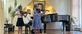 Na scenie auli PSM w Kłodzku dwie dziewczynki grają na skrzypcach, w tle na fortepianie akompaniuje P. Elżbieta Malinowska podczas Koncert uczniów klasy skrzypiec P. Krystyny Ślęzak - 14 maja 2024