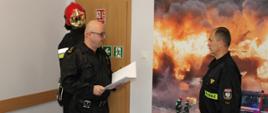 Z-ca Komendanta Powiatowego PSP w Nidzicy odczytuje list okolicznościowy z okazji 25-lecia pracy stojąc naprzeciwko wyróżnionego strażaka