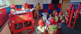 Zdjęcie przedstawia dzieci podczas zajęć w sali edukacyjnej z funkcjonariuszem PSP.