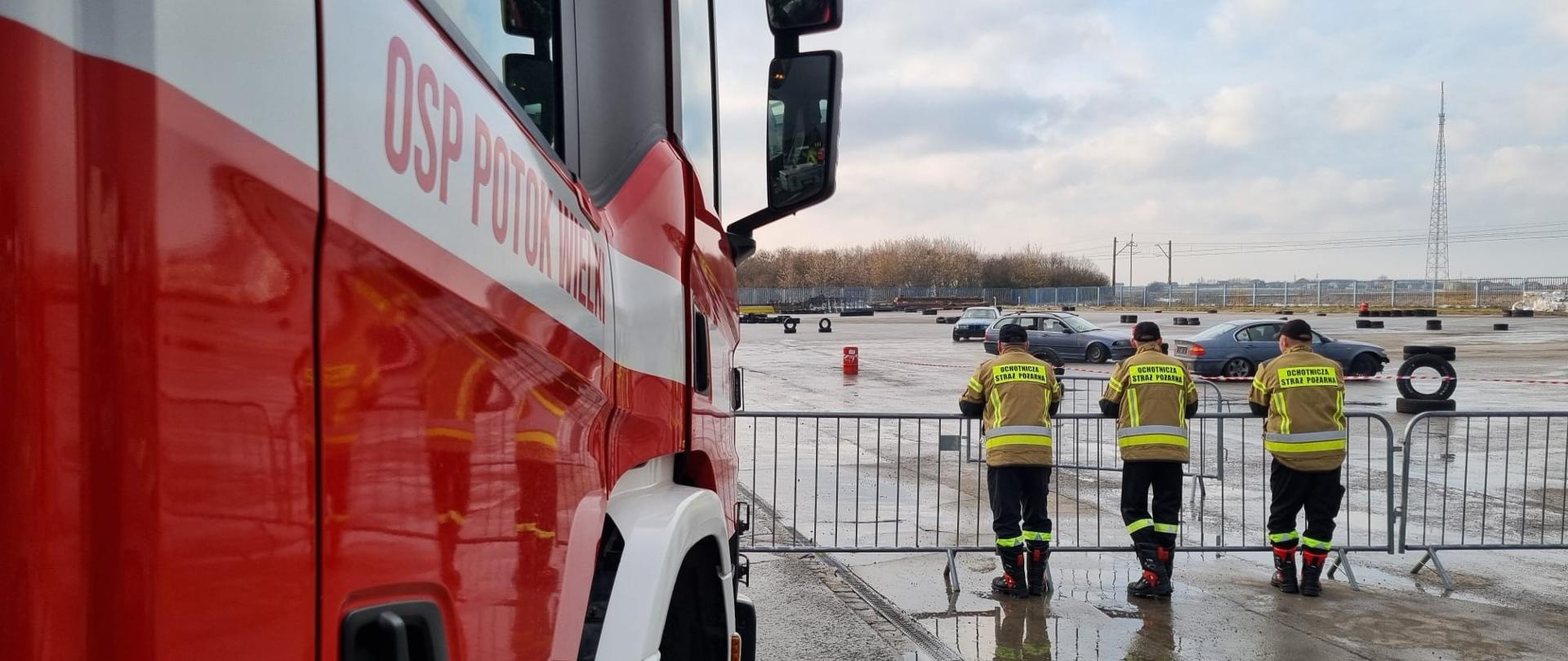 Na zdjęciu lewy prawy samochodu ratowniczo-gaśniczego. W tle strażacy odwróceni plecami do fotografa. Strażacy patrzą w stronę toru do pokazu dryftu i off-road’u.