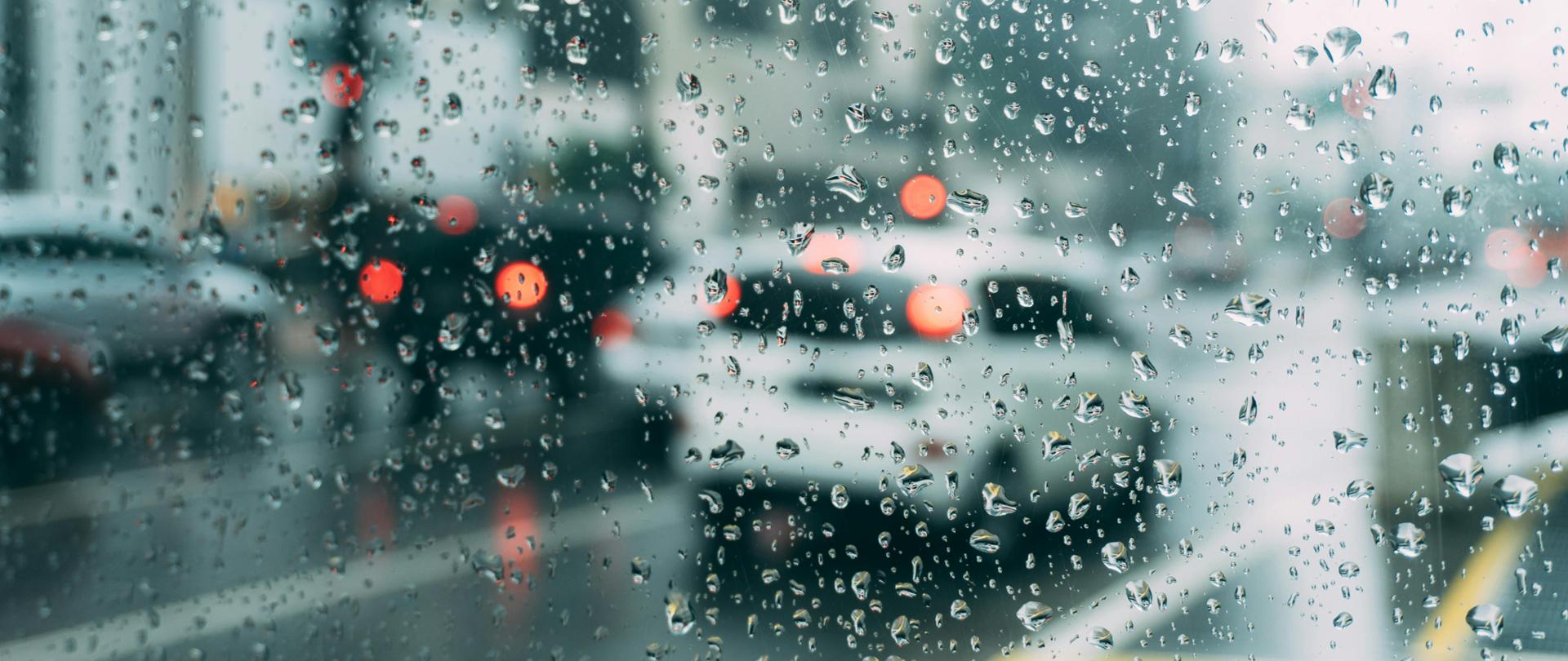 Zdjęcie przedstawia samochody za szybą w deszczu