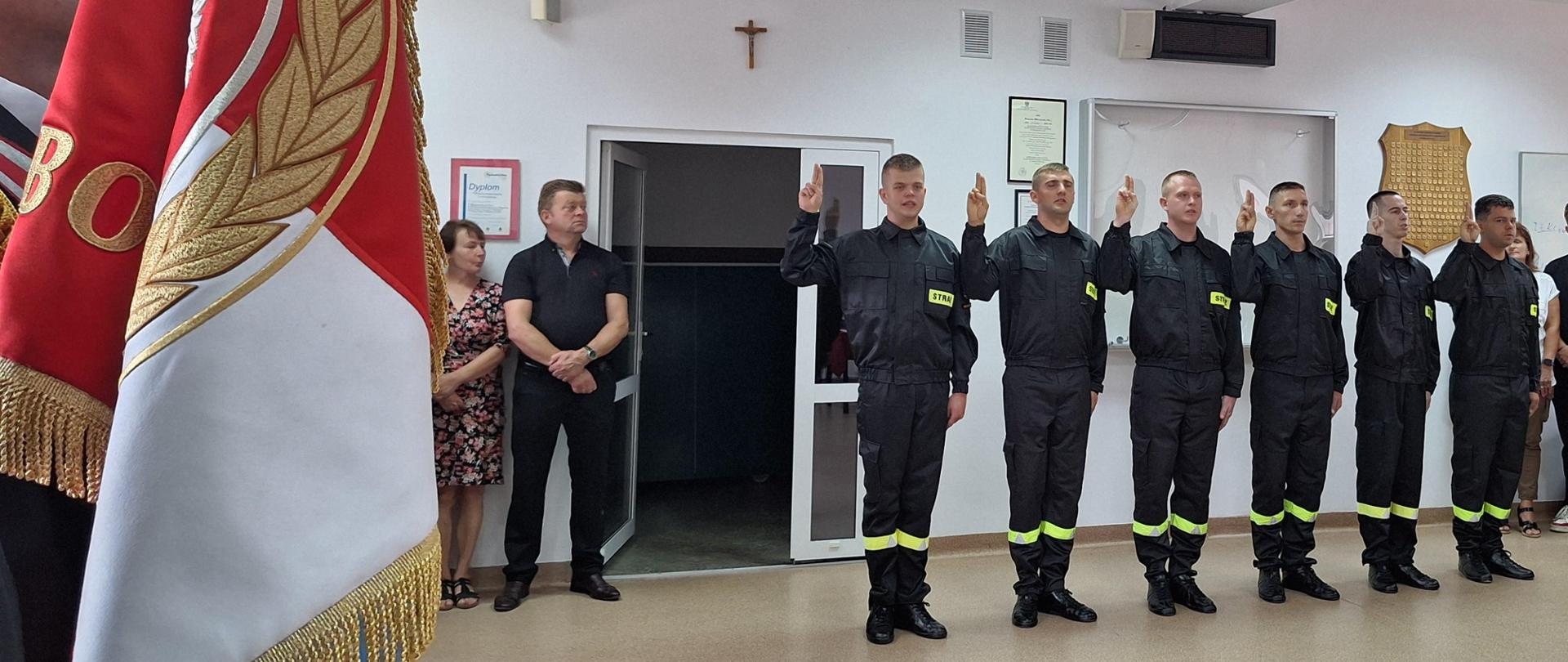 Strażacy stoją w szeregu z uniesiona prawa ręką do ślubowania