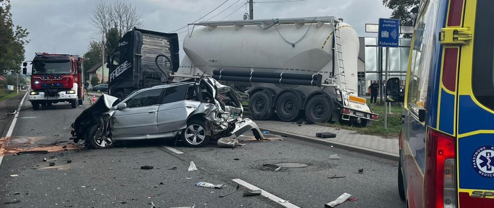  Ciągnik siodłowy z cysterną zlokalizowany jest częściowo na drodze, a tylna część naczepy w rowie, samochód osobowy znajduje się na środku drogi ustawiony w poprzek.