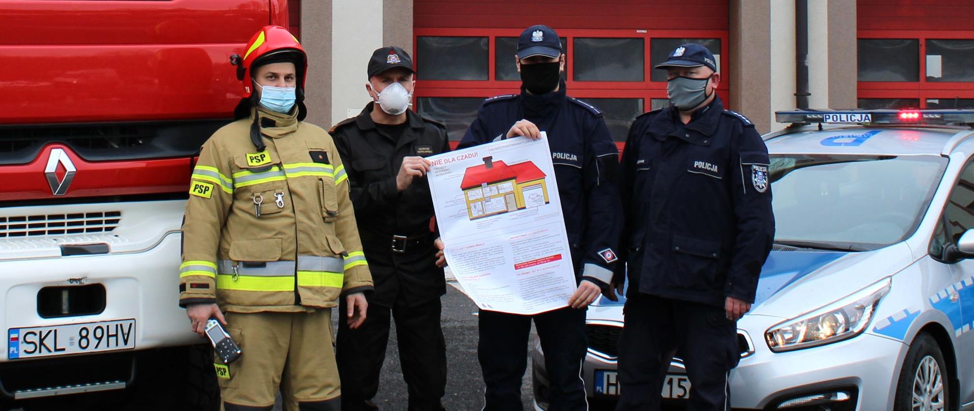 Zdjęcie przedstawia 2 strażaków z KP PSP w Kłobucku oraz dwóch policjantów z KPP w Kłobucku. Funkcjonariusze prezentują plakat wskazujący miejsca gdzie potencjalnie może powstać tlenek węgla.