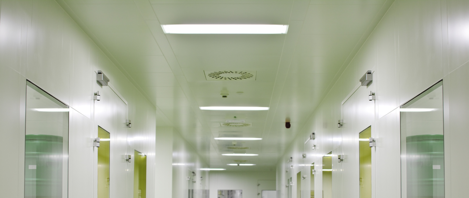 korytarz podmiotu leczniczego z białymi ścianami o drzwiami oraz widocznymi elementami wentylacji mechanicznej w suficie