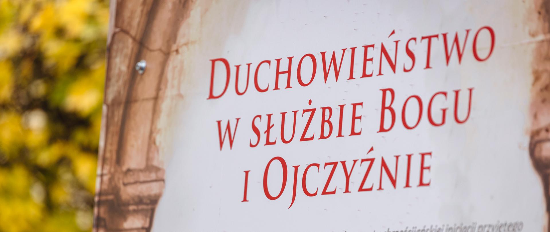 Tablica z czerwonym napisem na białym tle „Duchowieństwo w służbie Bogu i Ojczyźnie".