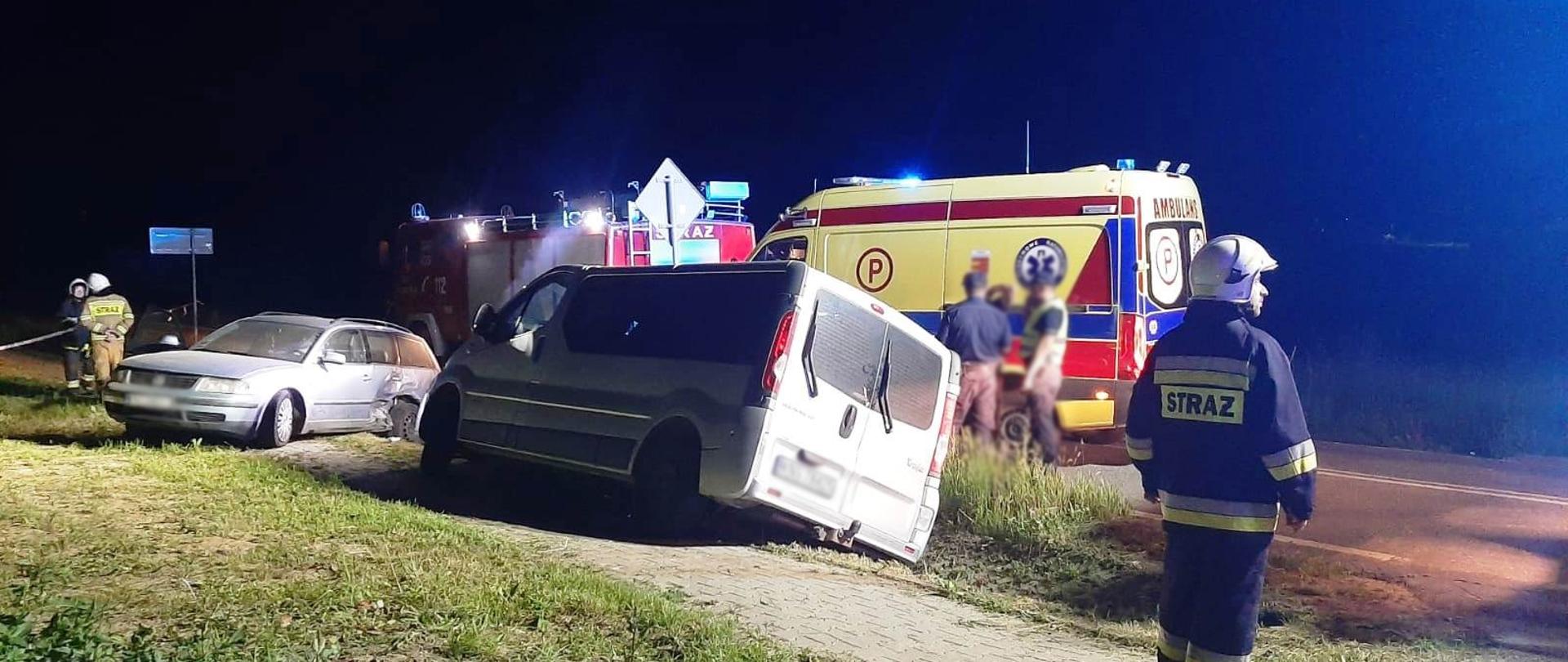 Samochód bus oraz samochod osobowy poza drogą. Obok nich strażacy. Na drodze karetka Pogotowia ratunkowego oraz samochód pożarniczy.