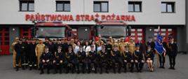 Zdjęcie grupowe strażaków i zaproszonych gości na tle komendy oraz samochodów pożarniczych