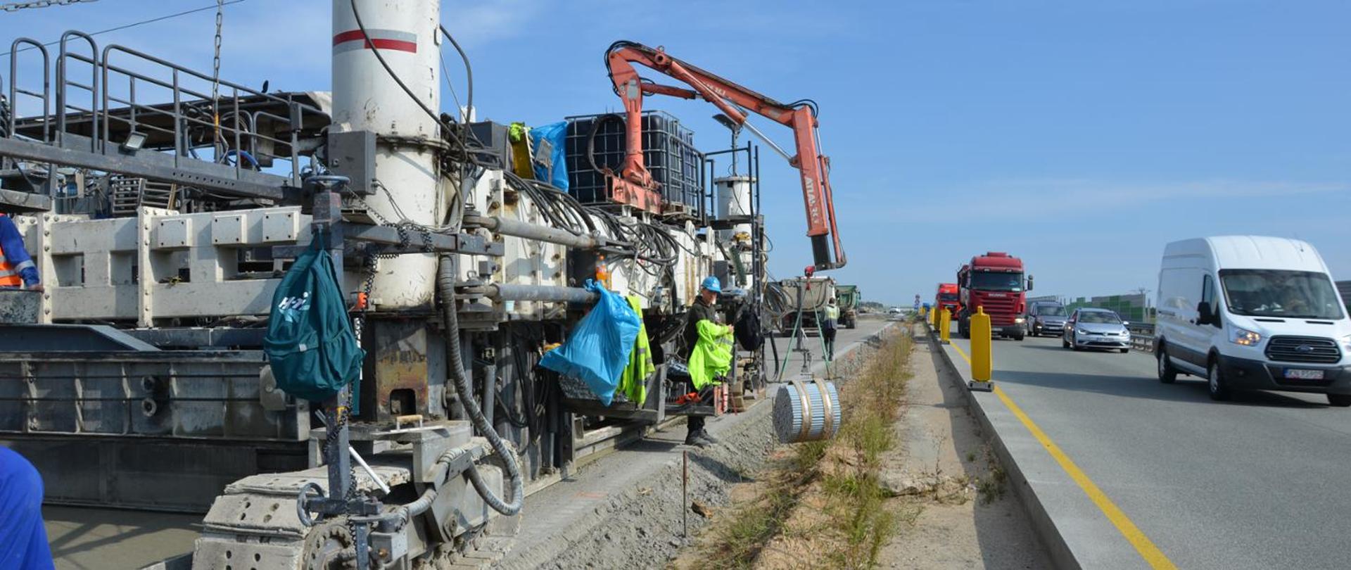 Po lewej stronie zdjęcia widoczna maszyna do układania nawierzchni betonowej na autostradzie A1. Po prawej jadące pojazdy.