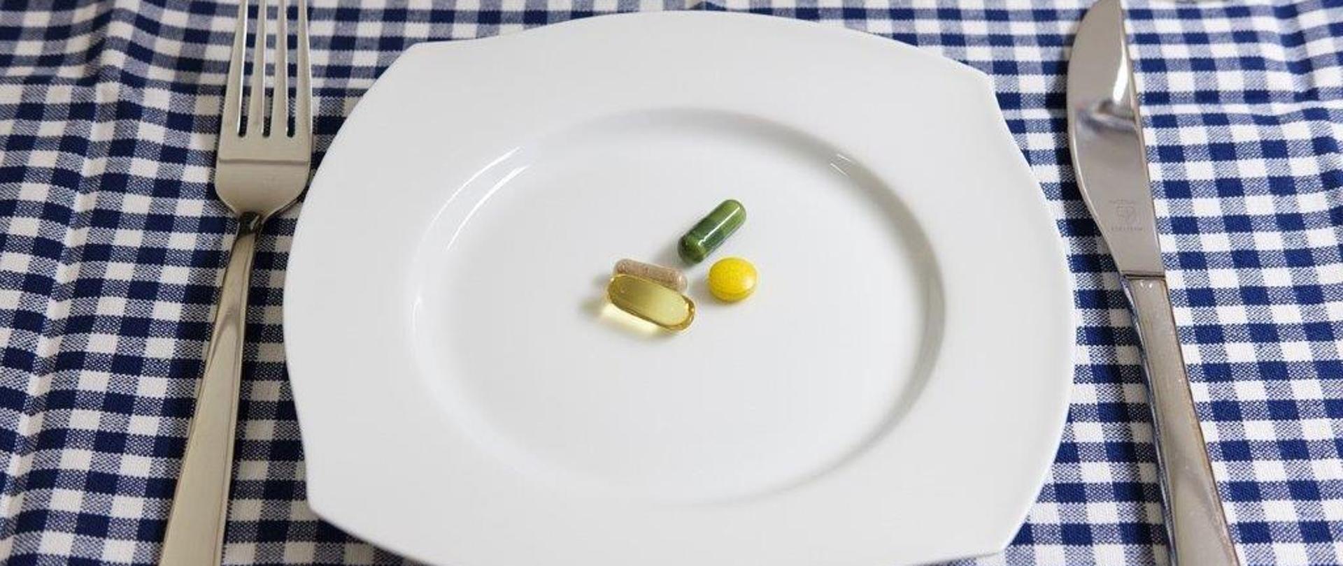 Suplementy diety w postaci tabletek i kapsułek na talerzu.