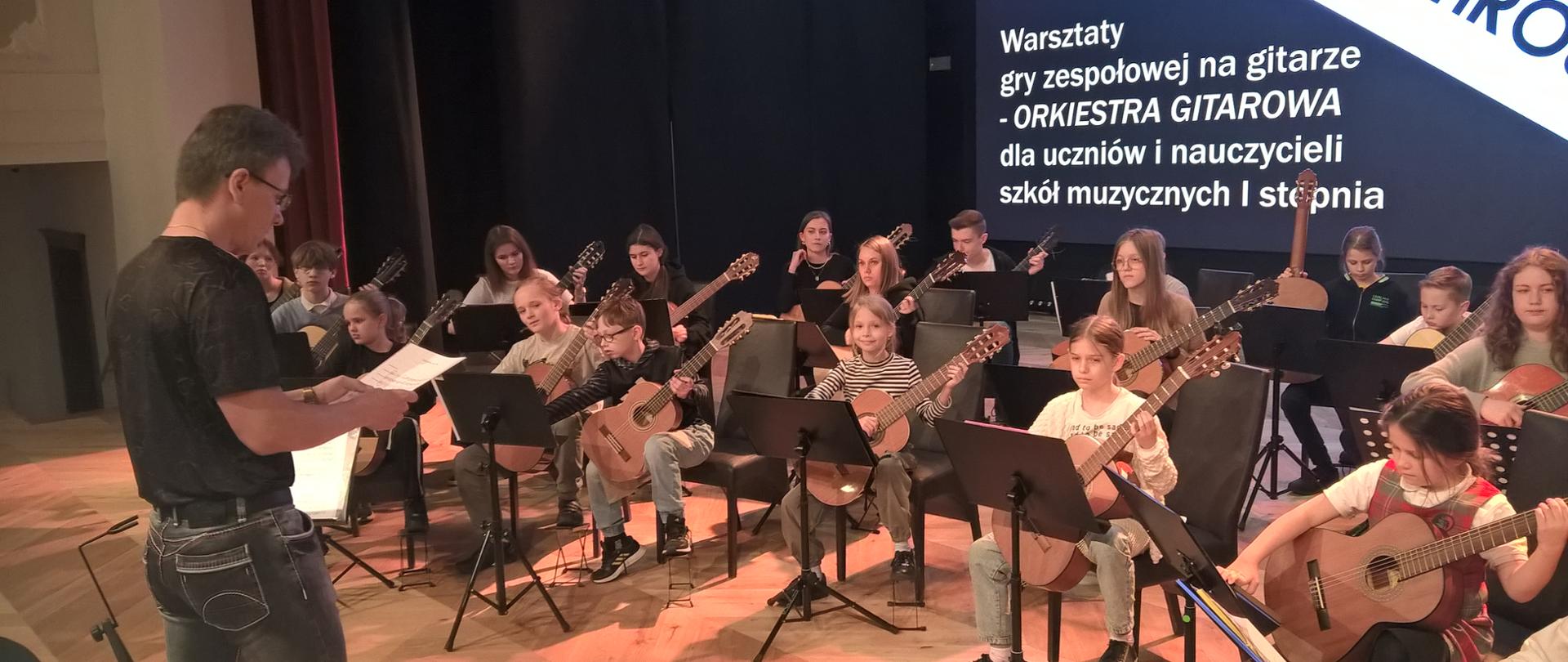 Orkiestra gitarowa na siedząca na scenie szkoły muzycznej w Śremie. 