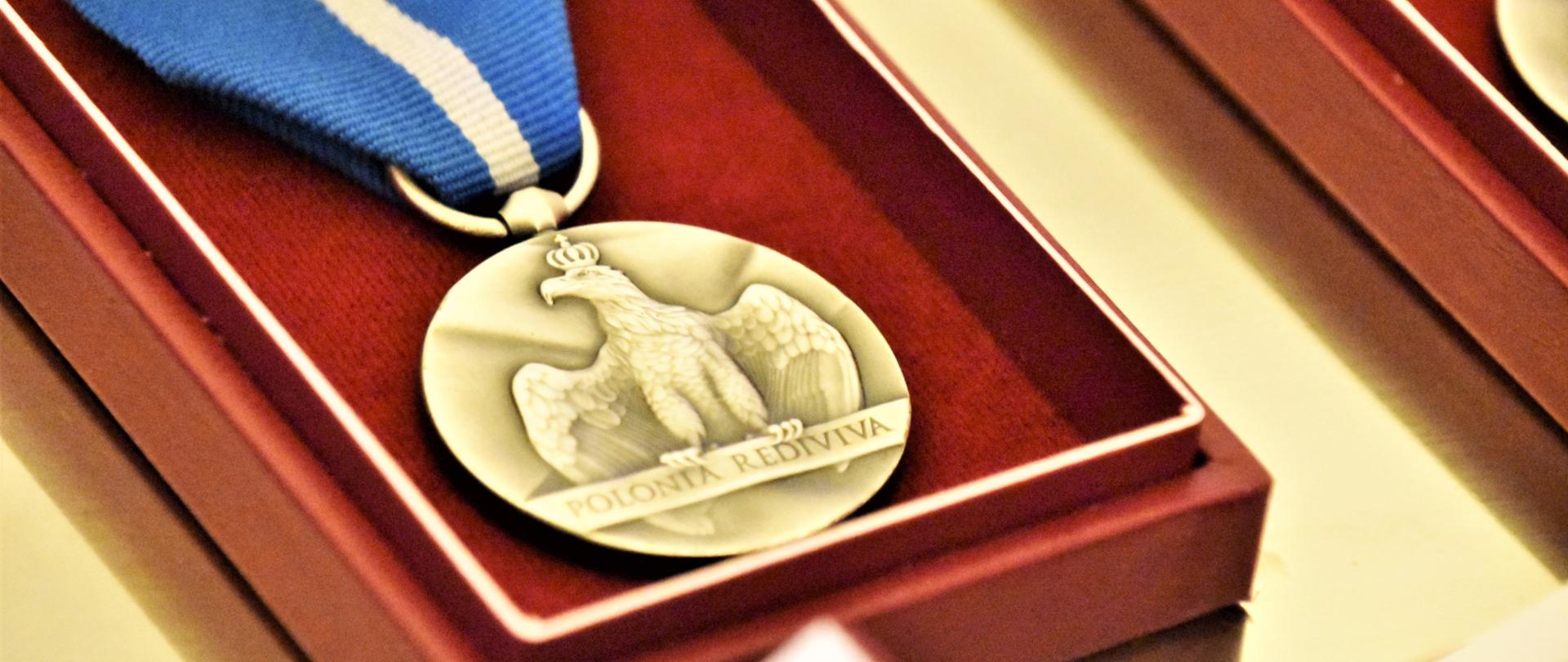 Na zdjęciu okrągły medal z umieszczonym pośrodku wizerunkiem orła wznoszącego skrzydła. Widnieje na nim napis POLONIA REDIVIVA (POLSKA ODRODZONA). Medal zawieszony jest na niebieskiej wstążce. 