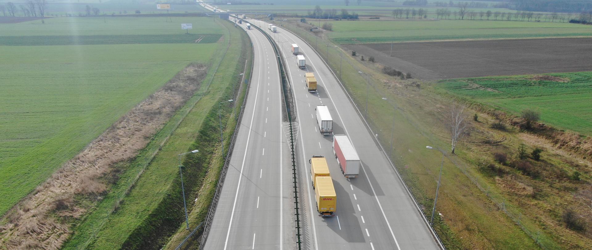 na zdjęciu widoczne dwie jezdnie autostrady, po której poruszają się pojazdy. Po obu stronach drogi łąki i pola