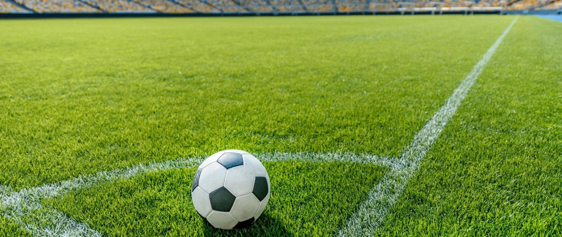 Na zdjęciu jest widoczna piłka nożna na murawie stadionu.