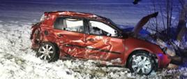 Zdjęcie przedstawia pomarańczowy samochód osobowy po zderzeniu bocznym. Cały bok auta jest rozbity, widać wystrzelone poduszki powietrzne w tym boczne. W tle widać pole pokryte śniegiem, zdjęcie zrobione nocą.