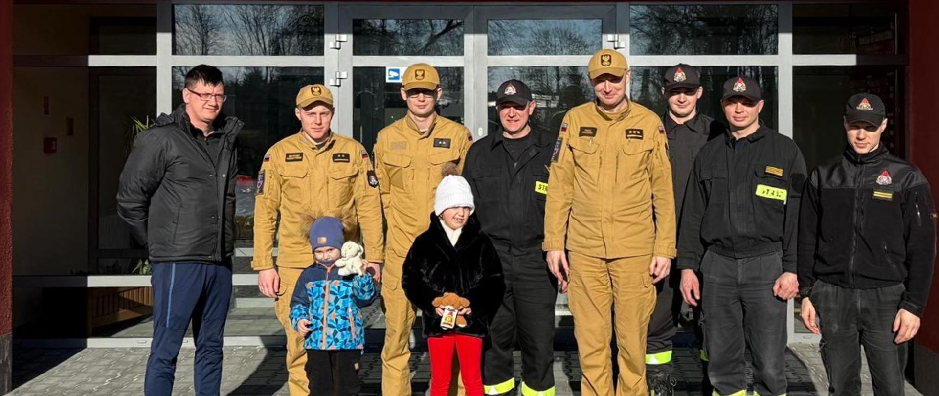 Osoby odwiedzające Komendę Powiatową Państwowej Straży Pożarnej w Turku pozują do zdjęcia razem ze strażakami. 