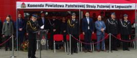 komendant powiatowy psp w legionowie przemawia przy mownicy. w tle pod czerwonym namiotem stoją zaproszeni goście.