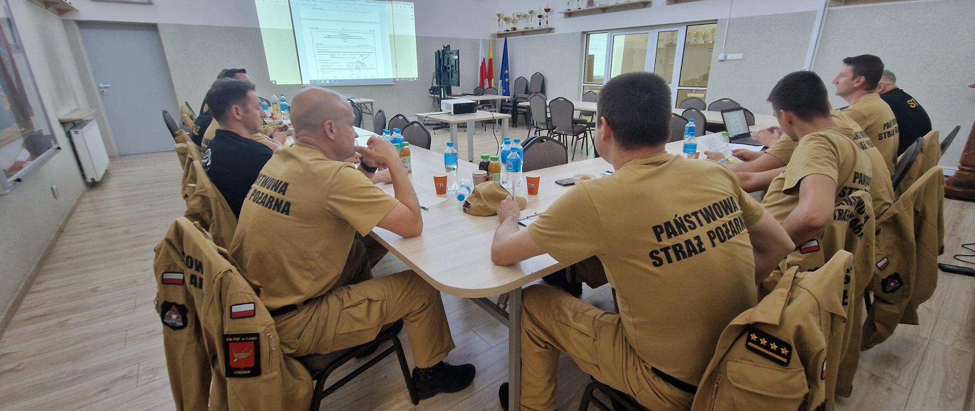 Strażacy PSP w mundurach służbowych siedzący przy stole konferencyjnym podczas odprawy