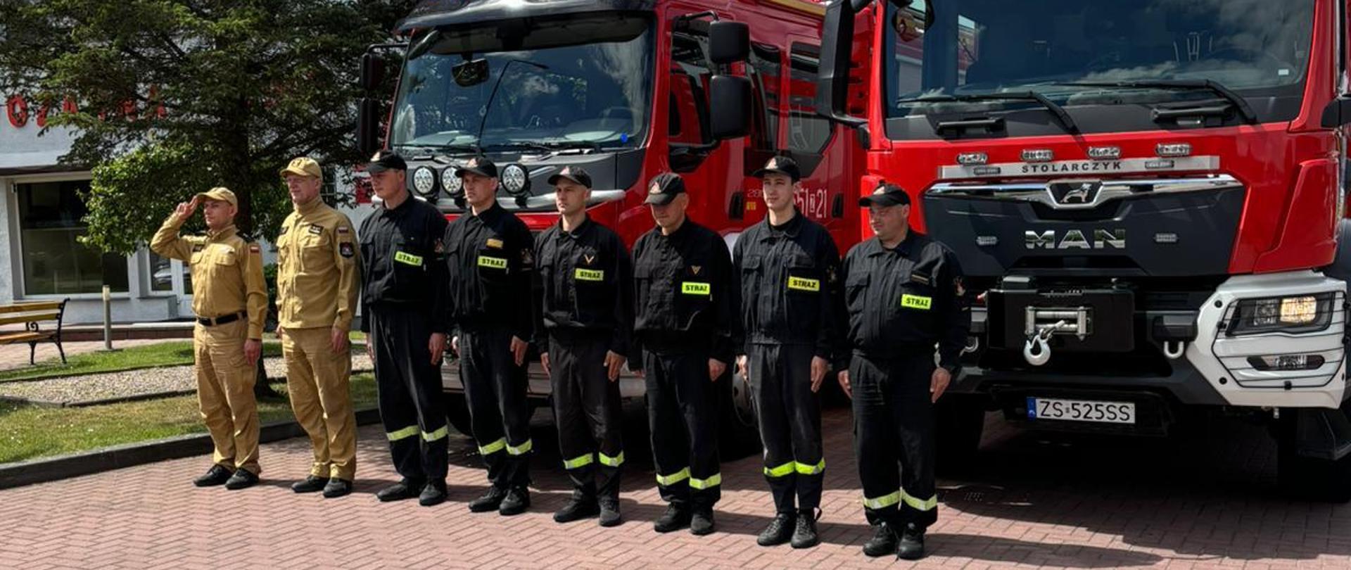 Zdjęcie przedstawia strażaków oddających hołd strażaków przy autach strażackich