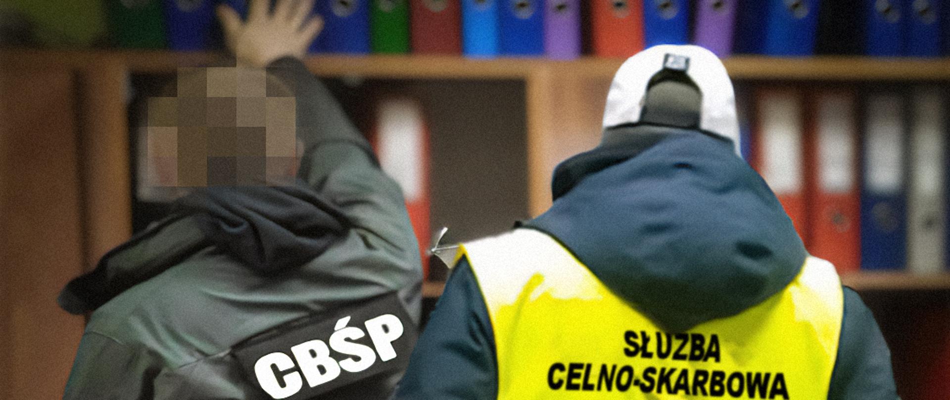 Funkcjonariusze CBŚP i Służby Celno-Skarbowej przy regale z segregatorami z dokumentami.