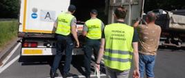 Pracownik Inspekcji Ochrony Środowiska, dwóch pracowników Służby Celno-Skarbowej oraz kierowca pojazdu stoją przy otwartych tylnych drzwiach naczepy.