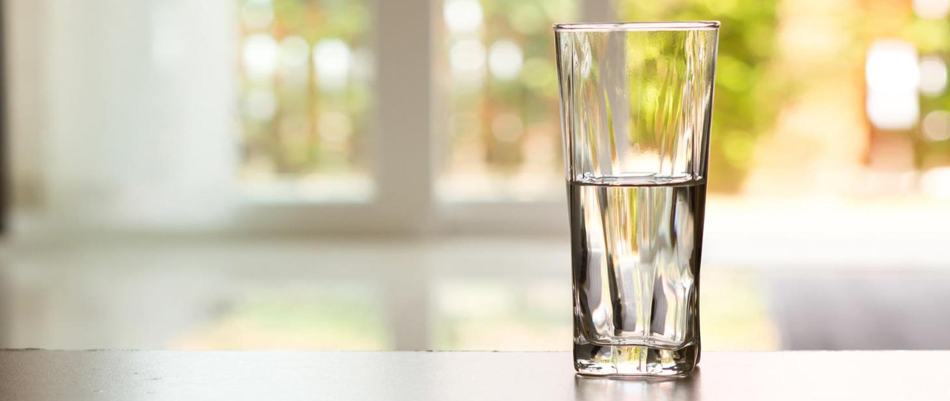 Na blacie po prawej stronie stoi szklanka do połowy wypełniona wodą