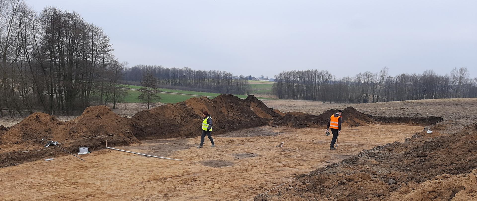 Budowa obwodnicy Opatowa - prace archeologiczne, odkryty pas ziemi, dwóch archeologów sprawdza teren