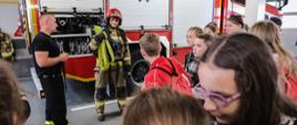 Strażak prezentuje ubranie do działań gaśniczych na tle samochodu pożarniczego