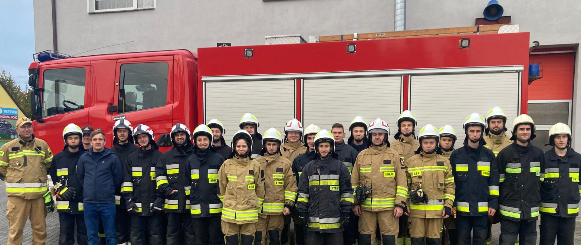 wspólne zdjęcie kursantów Ochotniczych straży pożarnych biorących udział w kursie, na tle samochodu ratowniczo gaśniczego. Kursanci w ubraniach specjalnych.