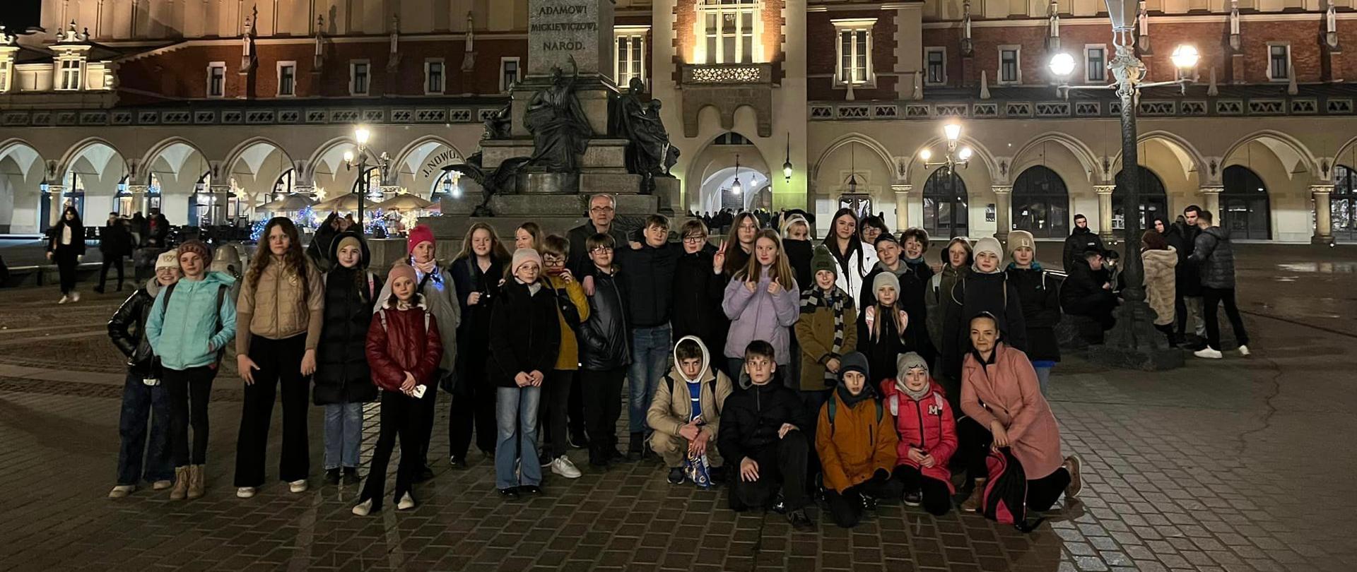 Zdjęcie grupy uczniów na tle Sukiennic w Krakowie zrobione nocą.