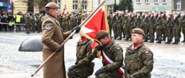 Dowódca 15. Lubuskiej Brygady Obrony Terytorialnej przekazuje Chorągiew Wojska Polskiego trzem klęczącym żołnierzom. Jeden z żołnierzy całuje Chorągiew. 