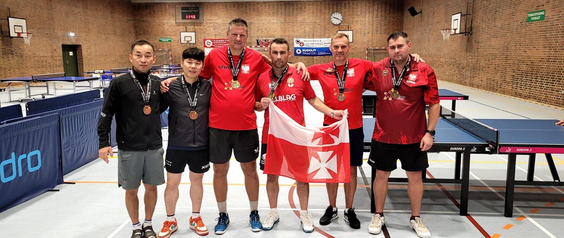 Hala sportowa. Sześciu zawodników w sportowych strojach z medalami an szyi.