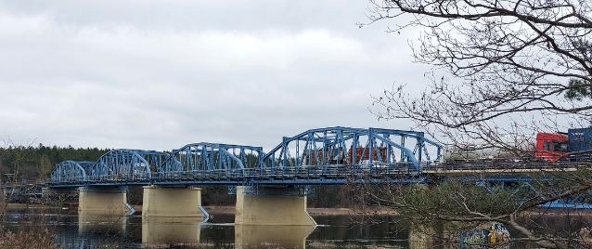 Stalowy most na betonowych podporach widziany znad brzegu rzeki