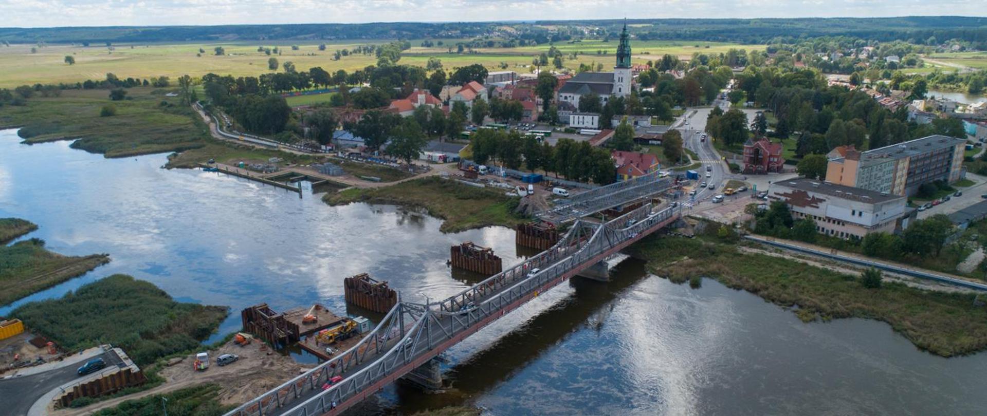 Wiosenny, słoneczny dzień. Widok z lotu ptaka na most nad rzeką, biegnący w stronę miejscowości.