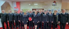 Funkcjonariusze i pracownicy Komendy Powiatowej Państwowej Straży Pożarnej w Jędrzejowie na uroczystej zbiórce pożegnania emerytów. Wszyscy znajdują się na sali tradycji.
