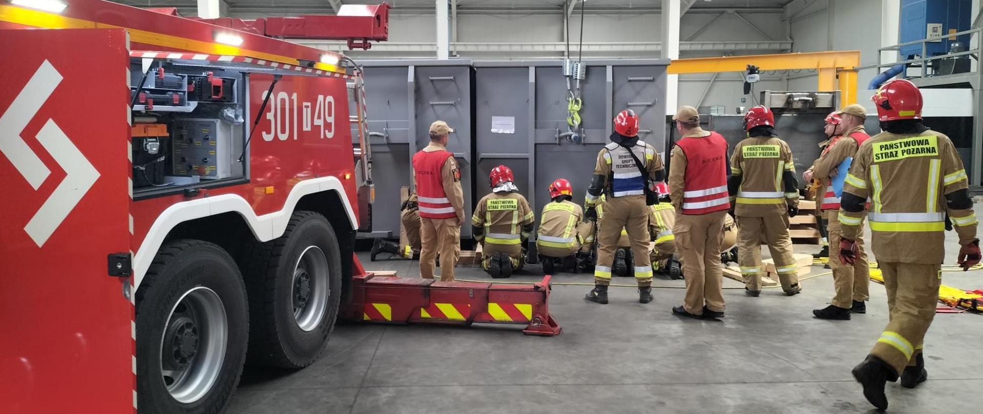Zdjęcie przedstawia strażaków podczas ćwiczeń w hali. Wydobycie poszkodowanego spod kontenera.