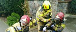 Na zdjęciu widzimy 2 strażaków zdejmujących zużyte przy działaniach aparaty powietrzne oraz strażaka pomagającego im je zdjąć.