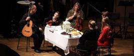 Rodzina przy wigilijnym stole, dzieci, rodzice, goście. Instrumenty - skrzypce, gitara
