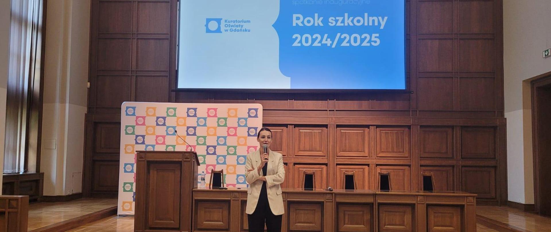 kobieta (wojewoda) stoi w dużej sali i przemawia, za nią tablica z napisem rok szkolny 20245/2025