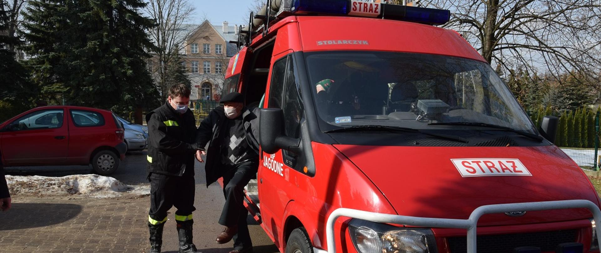 strażak pomaga wysiąść z pojazdu pożarniczego mężczyźnie