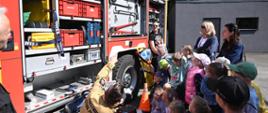 Strażak prezentuje dzieciom sprzęt ratowniczy na samochodzie pożarniczym
