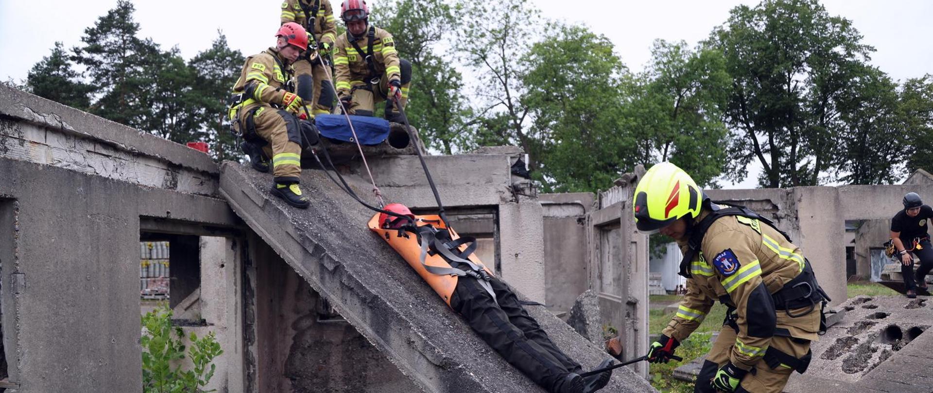 Ćwiczący strażacy ewakuują z gruzowiska na noszach SKED osobę poszkodowaną (symulowaną przez fantom ratowniczy)